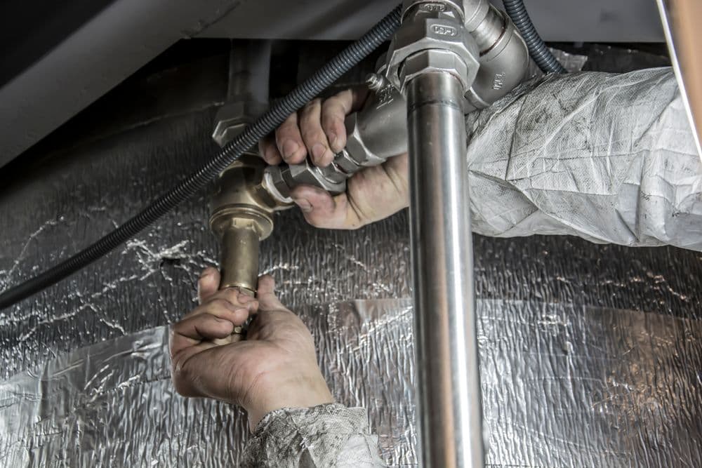A plumber's hands tightening a pipe fitting under a sink